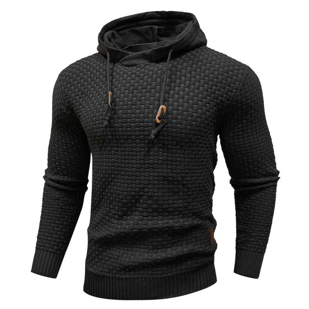Mannelijk model draagt de Siebe hoodie in zwart, vooraanzicht, staand in een stedelijke omgeving met bakstenen muur.
