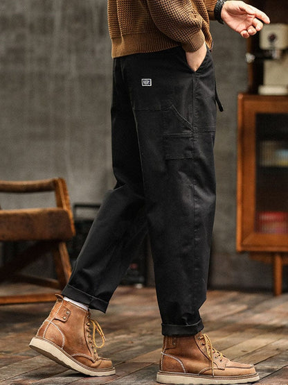 Een model staat relaxed met de handen in de zakken van de zwarte utility broek, toont de casual stijl.