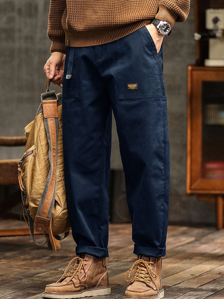 Model leunt tegen een muur in de legergroene broek, een lifestyle shot dat de alledaagse draagbaarheid illustreert.