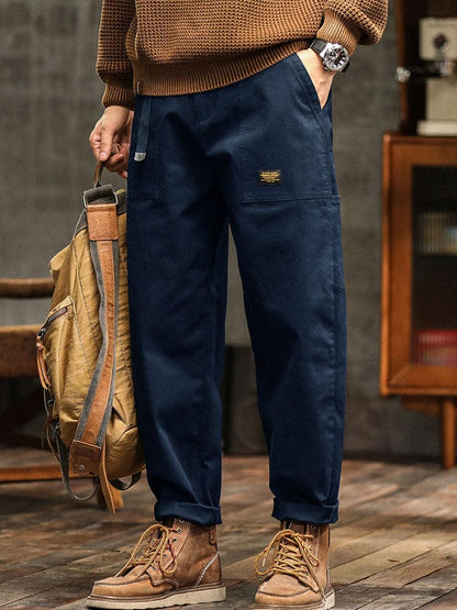 Model leunt tegen een muur in de legergroene broek, een lifestyle shot dat de alledaagse draagbaarheid illustreert.