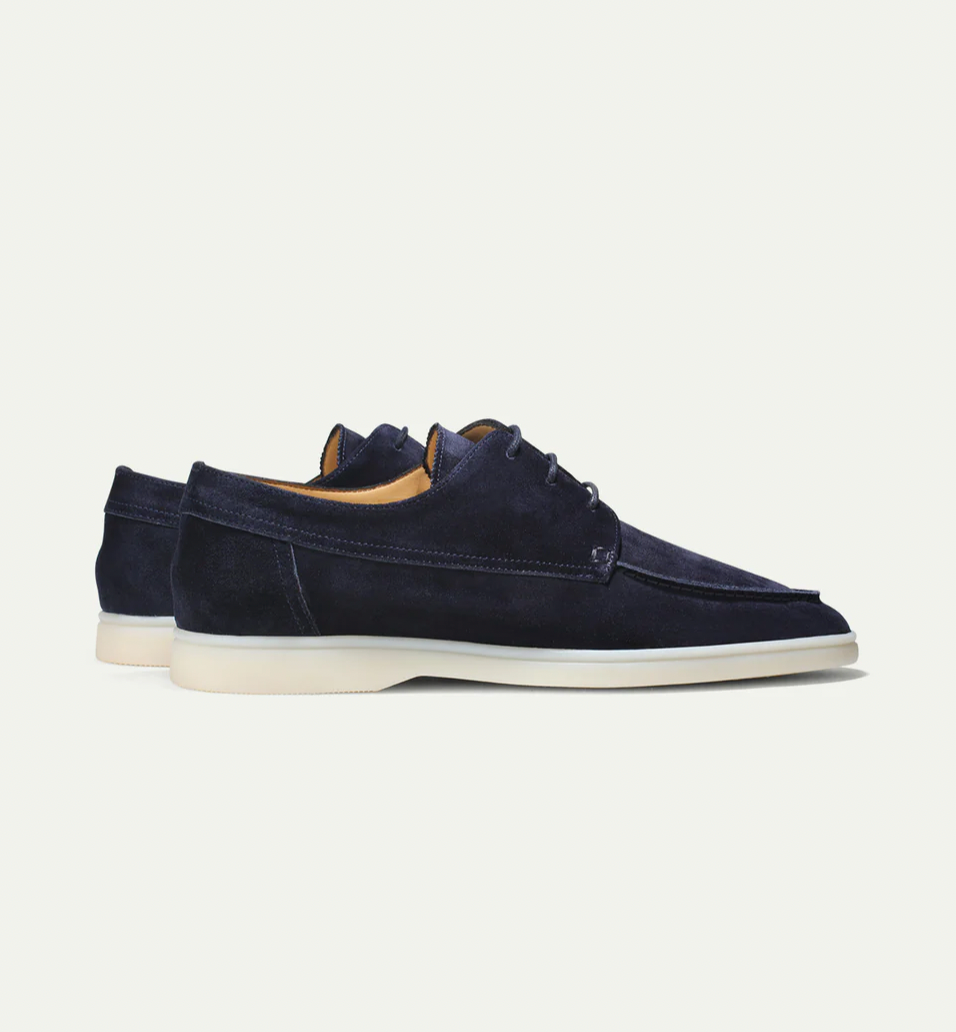Zijaanzicht van de lichtbeige suède loafers, met de flexibele rubberen zool duidelijk zichtbaar op een lichte vloer.