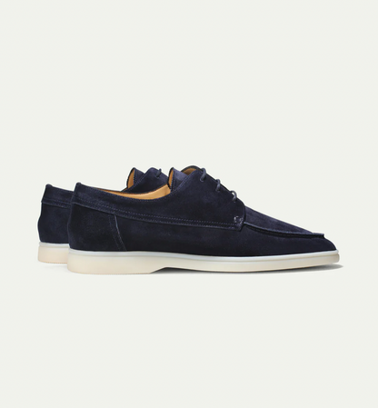 Zijaanzicht van de lichtbeige suède loafers, met de flexibele rubberen zool duidelijk zichtbaar op een lichte vloer.