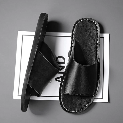 Een paar zwarte leren sandalen gepresenteerd in een minimalistische studio-omgeving.