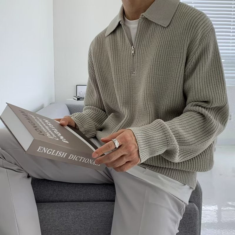Een man draagt de zwarte half-zip trui in een casual setting, zittend en ontspannen met een open boek.