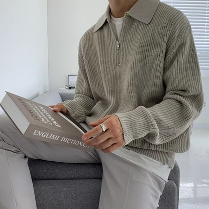 Een man draagt de zwarte half-zip trui in een casual setting, zittend en ontspannen met een open boek.