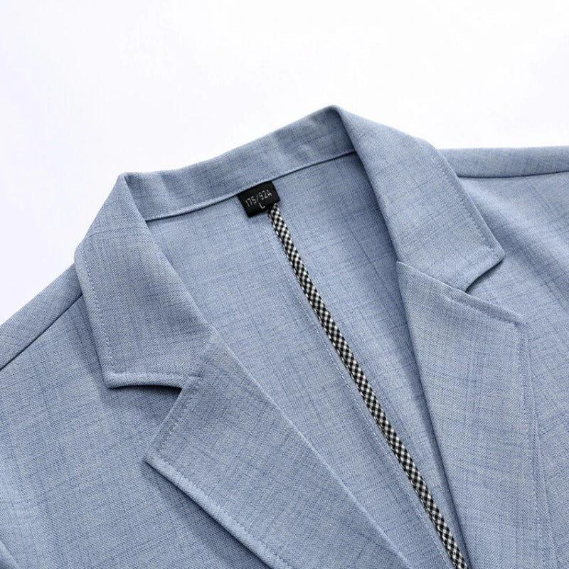 De herenblazer in beige, plat gelegd om de kreukvrije eigenschappen en het lichte gewicht van de stof te benadrukken.