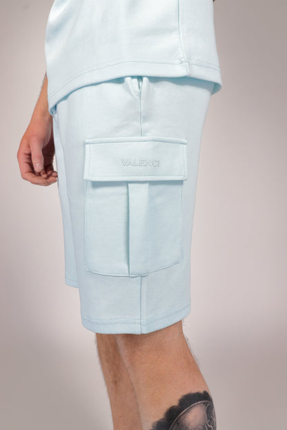 Model draagt de lichtblauwe cargo shorts in een ontspannen setting, zittend op een bankje.