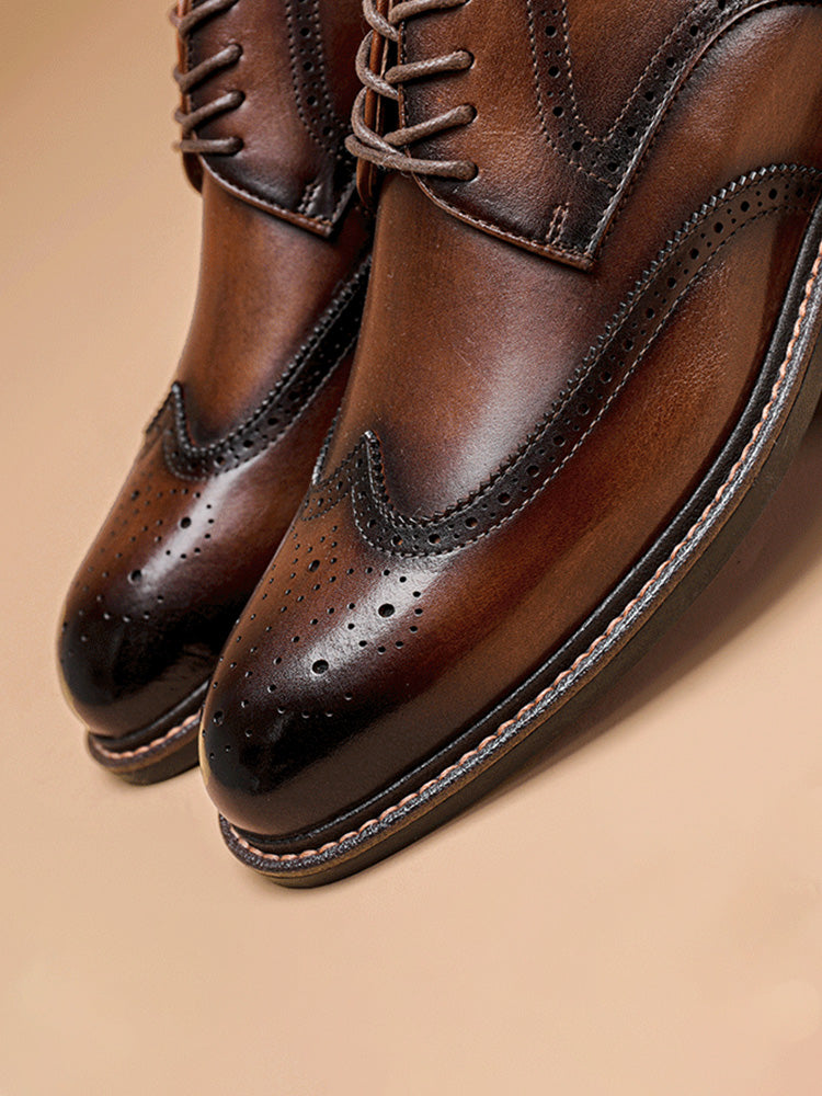 Een man zit gekleed in een kostuum, met de zwarte Wingtip Brogue herenschoenen prominent in beeld, straalt vertrouwen uit.