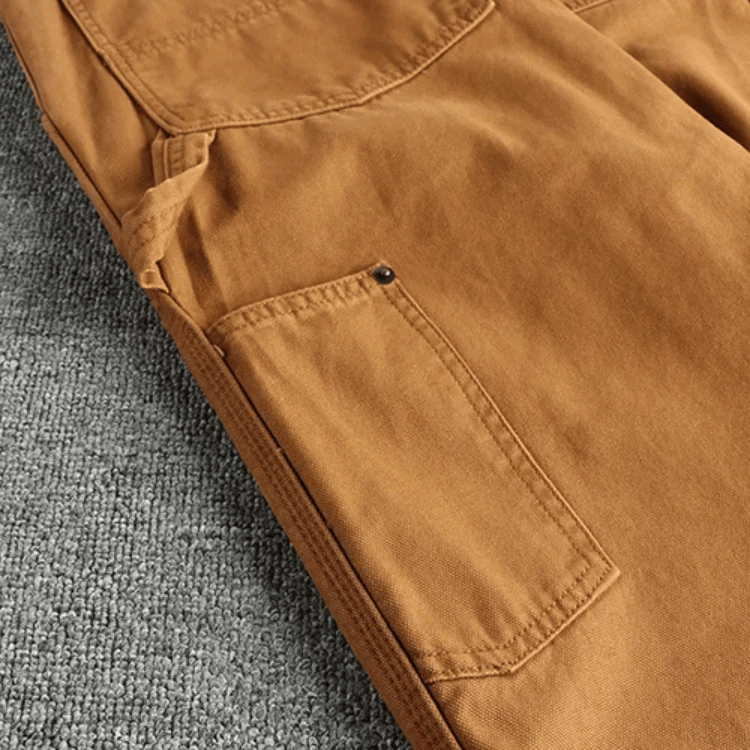 De utility broek plat gelegd, met aandacht voor de tailleband, knoopsluiting en de algehele vorm.