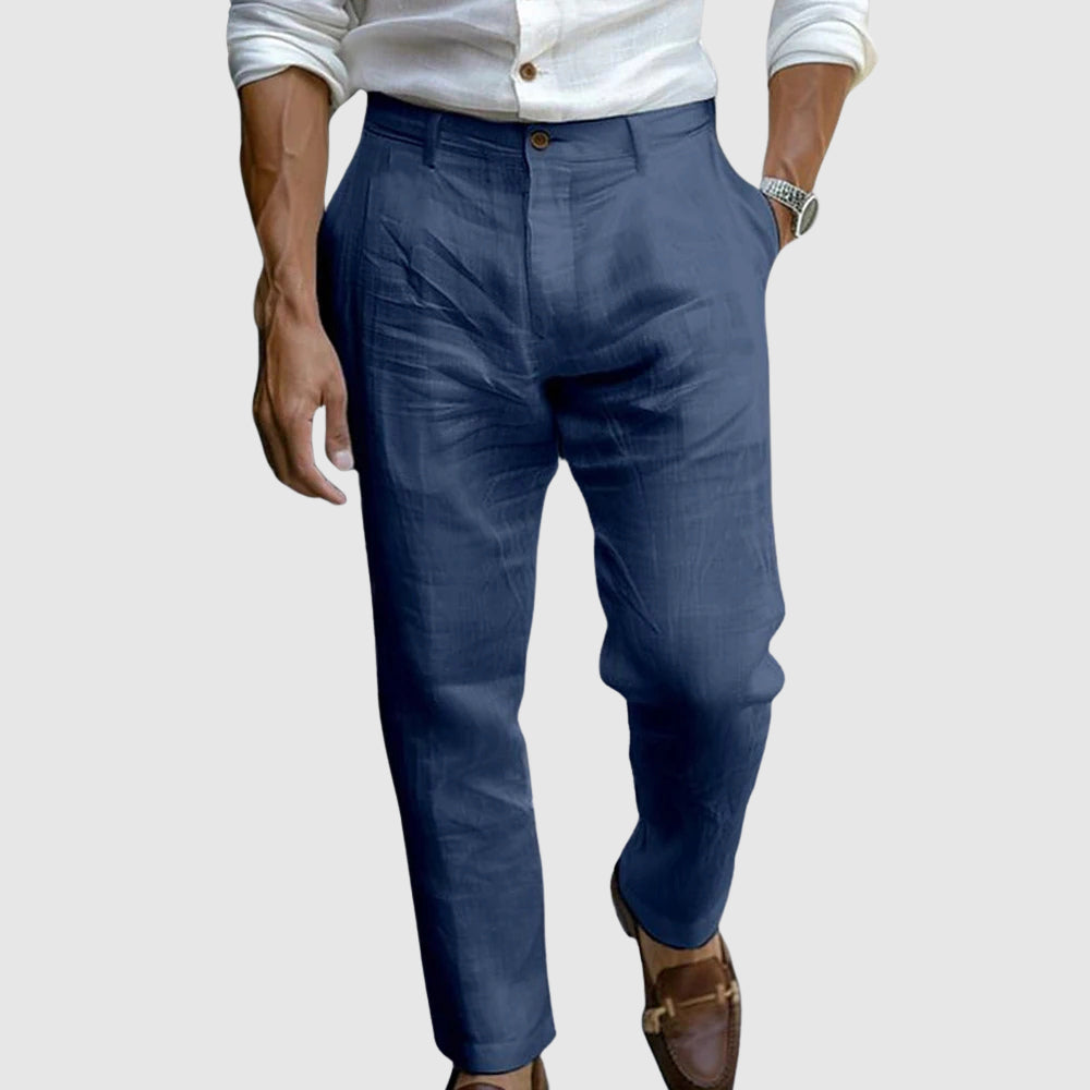 Een model draagt een blauwe linnen broek in een stedelijke omgeving, wat de geschiktheid voor zowel casual als smart casual gelegenheden laat zien.