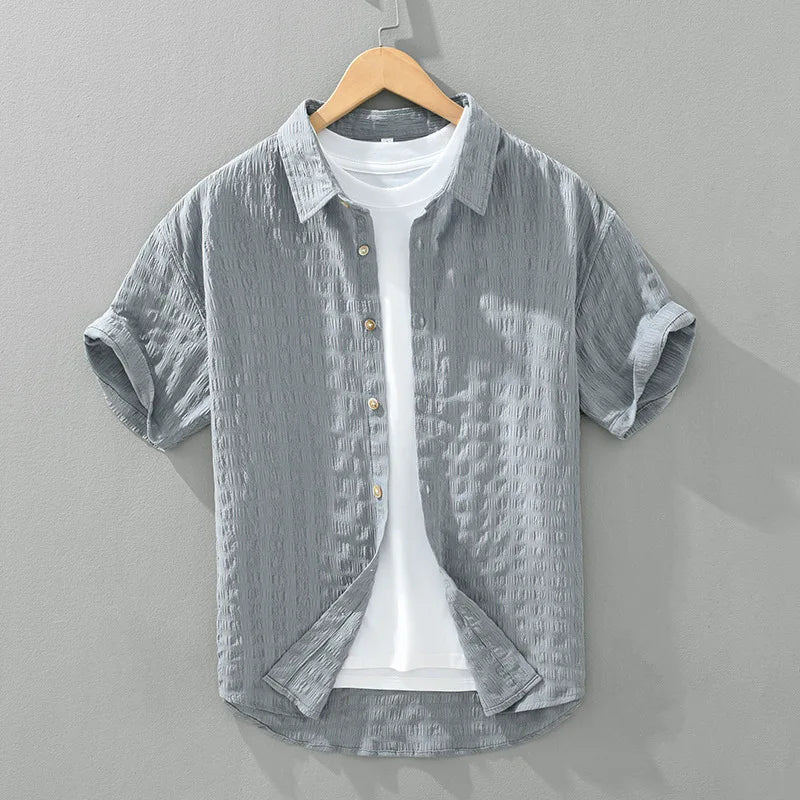 Een man draagt een grijs heren overhemd in een ontspannen zomerse setting, perfect voor comfort en stijl.