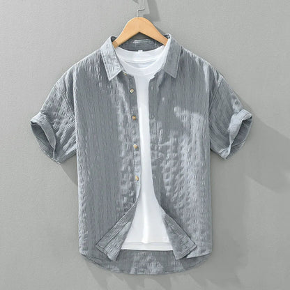 Een man draagt een grijs heren overhemd in een ontspannen zomerse setting, perfect voor comfort en stijl.