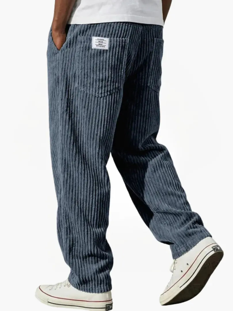 Man draagt de Jonas corduroy broek in blauw, staand in een ontspannen, casual pose.
