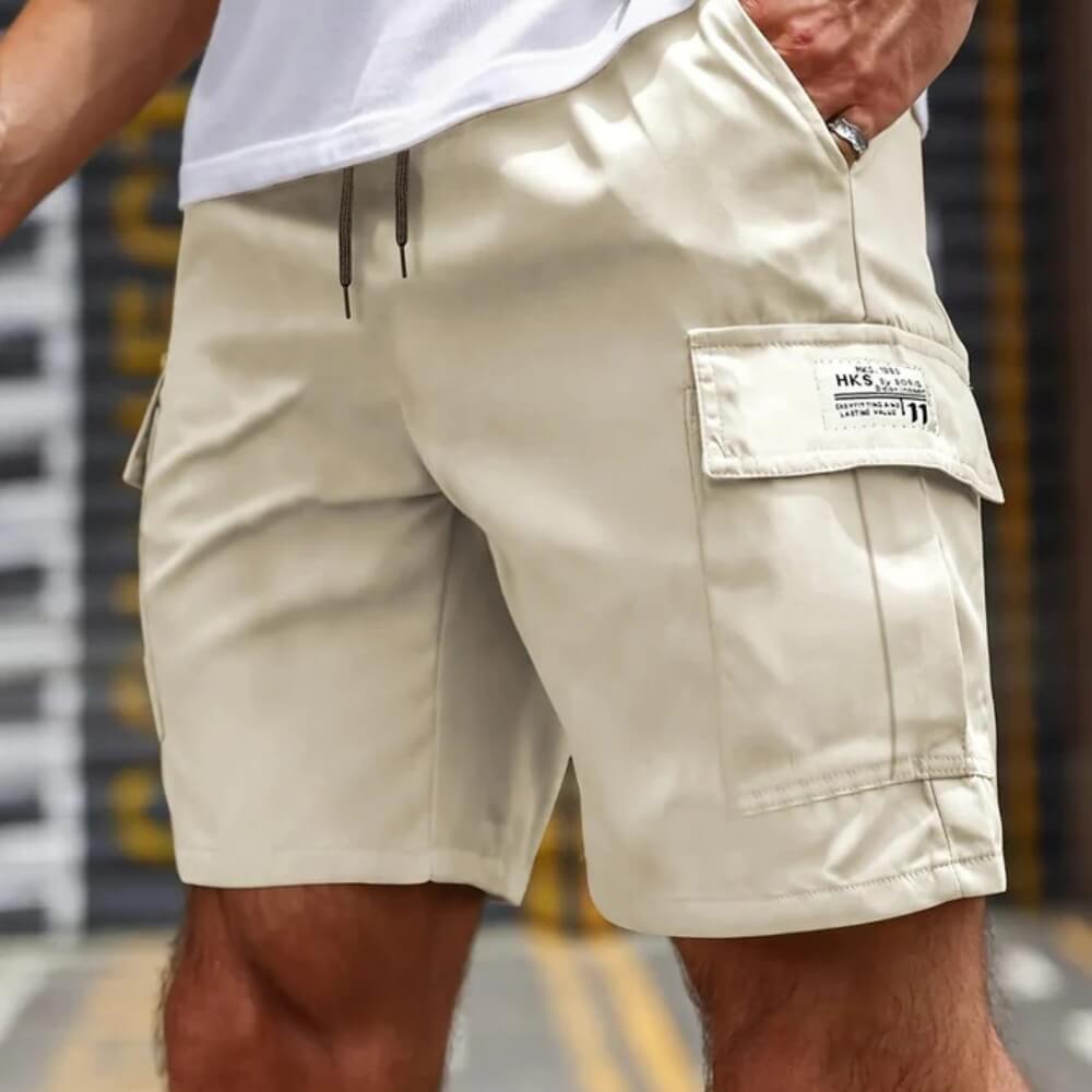 Model dat de Jorin cargoshorts voor heren draagt in een lichte tint, staand in een stedelijke omgeving.