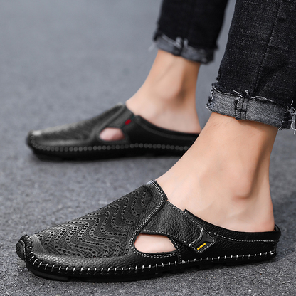 Een paar Julian leren sandalen in een lichte tint, gefotografeerd vanuit een lage hoek, op een zandkleurige ondergrond.