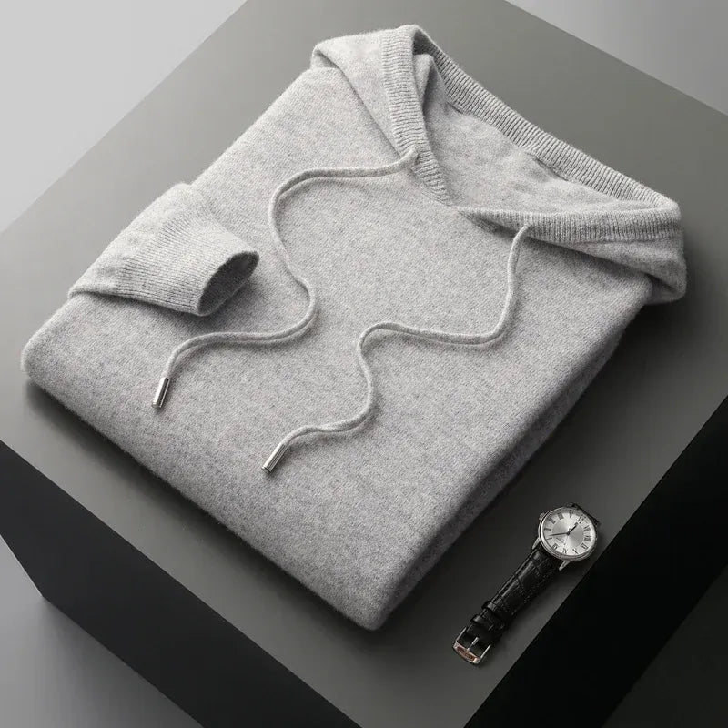 Man in een sage-kleurige merinowollen hoodie, genietend van een moment van ontspanning binnenshuis.