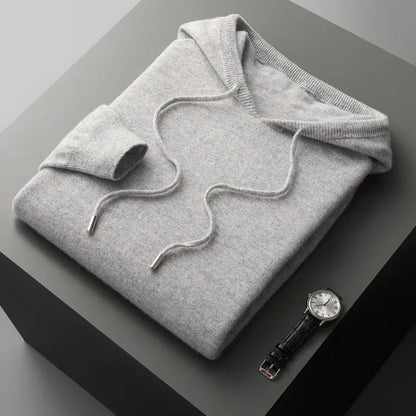 Man in een sage-kleurige merinowollen hoodie, genietend van een moment van ontspanning binnenshuis.