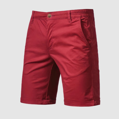 Een man zit op een terras en geniet van een drankje, gekleed in de stijlvolle Loris katoenen shorts.