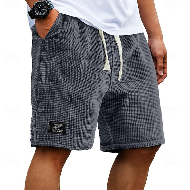 Vooraanzicht van de Nils wafelkatoenen shorts in grijs, gedragen door een man in een ontspannen setting.