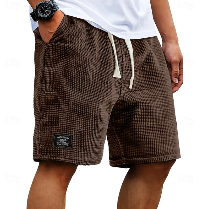 Een stapel Nils wafelkatoenen shorts in verschillende kleuren: zwart, bruin, groen en blauw.