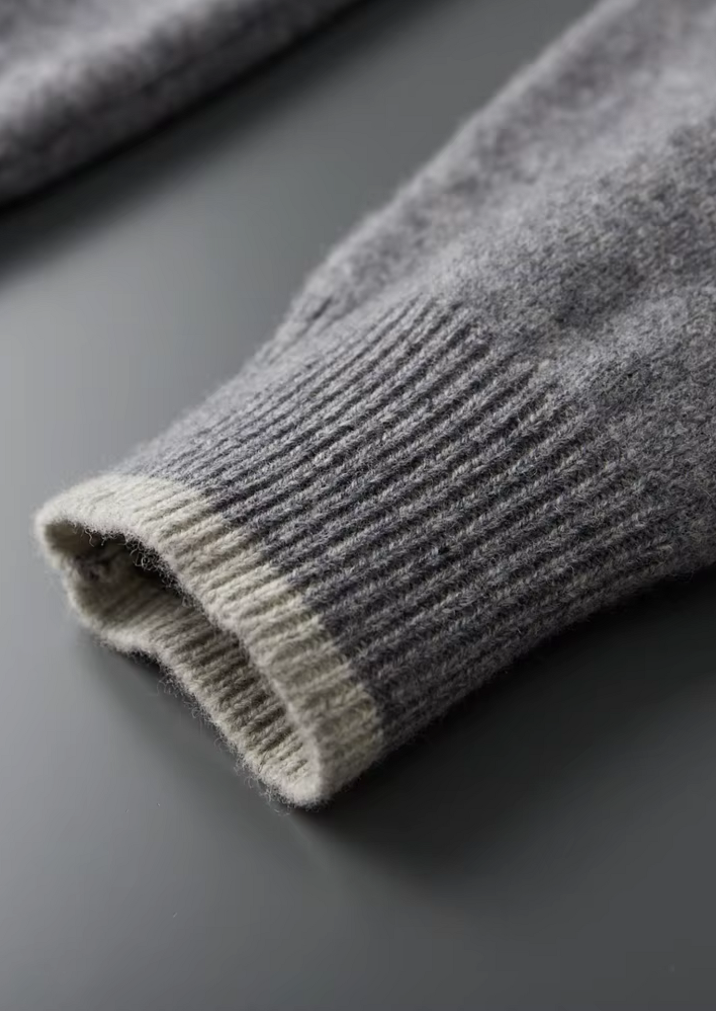 Detail van de soepele ritssluiting en de subtiele tweekleurige rand van de grijze cardigan.