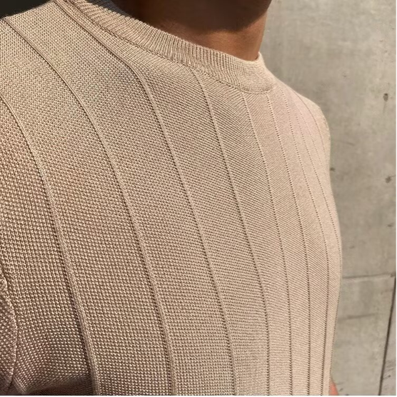Close-up van de ronde halslijn en de korte mouw van het stijlvolle beige Reuben T-shirt.