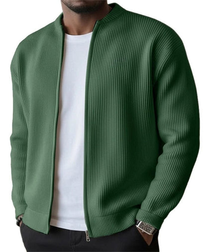 Mannelijk model draagt de olijfgroene gebreide jas met ritssluiting, zittend, toont de veelzijdigheid en het comfort.